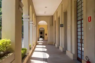 Ilustrasi: Lorong gedung dengan pilar-pilar melengkung dan lantai berpenerangan alami yang sepi.