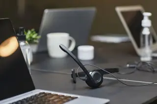 Ilustrasi: Headset dengan mikrofon dan laptop di atas meja kerja kantor.