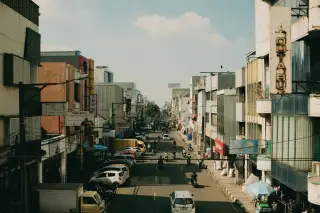 Ilustrasi: Pemandangan jalan perkotaan di Indonesia dengan deretan ruko, kabel melintang, dan kendaraan melintas.