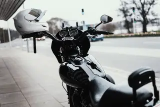 Ilustrasi: Sepeda motor hitam terparkir di trotoar dengan helm putih tergantung di stang.