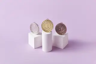 Ilustrasi: Tiga medali bertuliskan angka satu dua dan tiga di atas podium putih berlatar ungu.