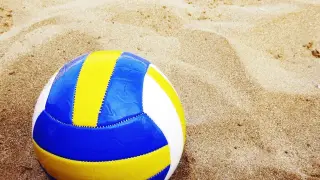 Ilustrasi: Sebuah bola voli berwarna biru, kuning, dan putih tergeletak di atas pasir pantai.