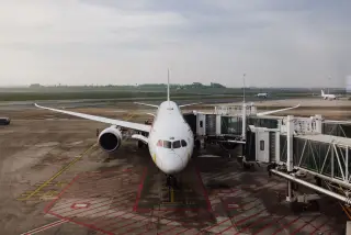 Ilustrasi: Pesawat penumpang terparkir di garbarata terminal bandara di bawah langit berawan.