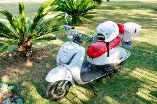 Ilustrasi: Sepeda motor skuter putih terparkir di taman dengan helm putih diletakkan di atas jok.