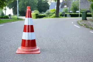 Ilustrasi: Sebuah kerucut lalu lintas berwarna merah putih berdiri di atas jalan aspal.