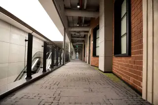 Ilustrasi: Lorong bangunan modern yang sepi dan bersih dengan dinding bata serta eskalator di sisi samping.